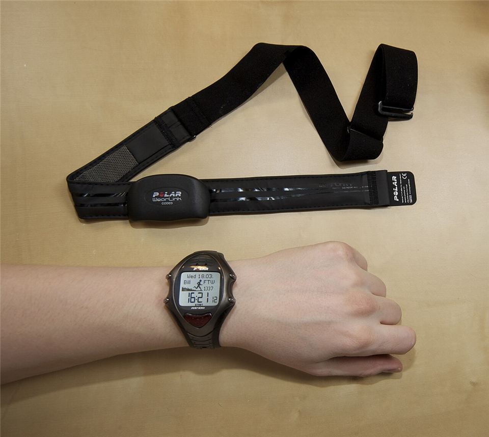 A heart rate monitor chest strap lying on a table above a wrist wearing the matching training watch