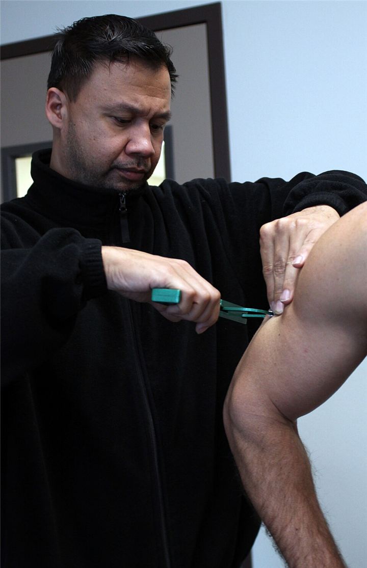 A fitness supervisor pinches a fold of skin on the back of a man’s upper arm and measures it with a green plastic skinfold caliper