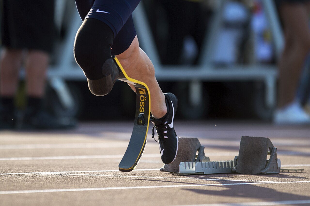 A sprinter with a prosthetic running blade pushing off from starting blocks on a track