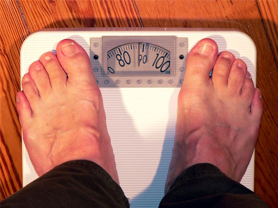 Bare feet standing on an analog bathroom scale whose dial reads between 80 and 100